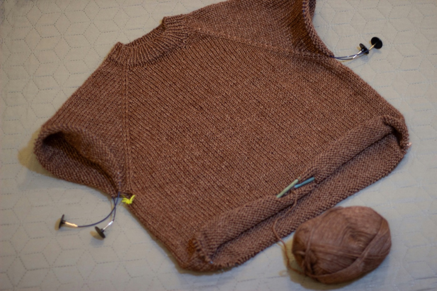 A half-finished brown knitted sweater with needles and a ball of yarn